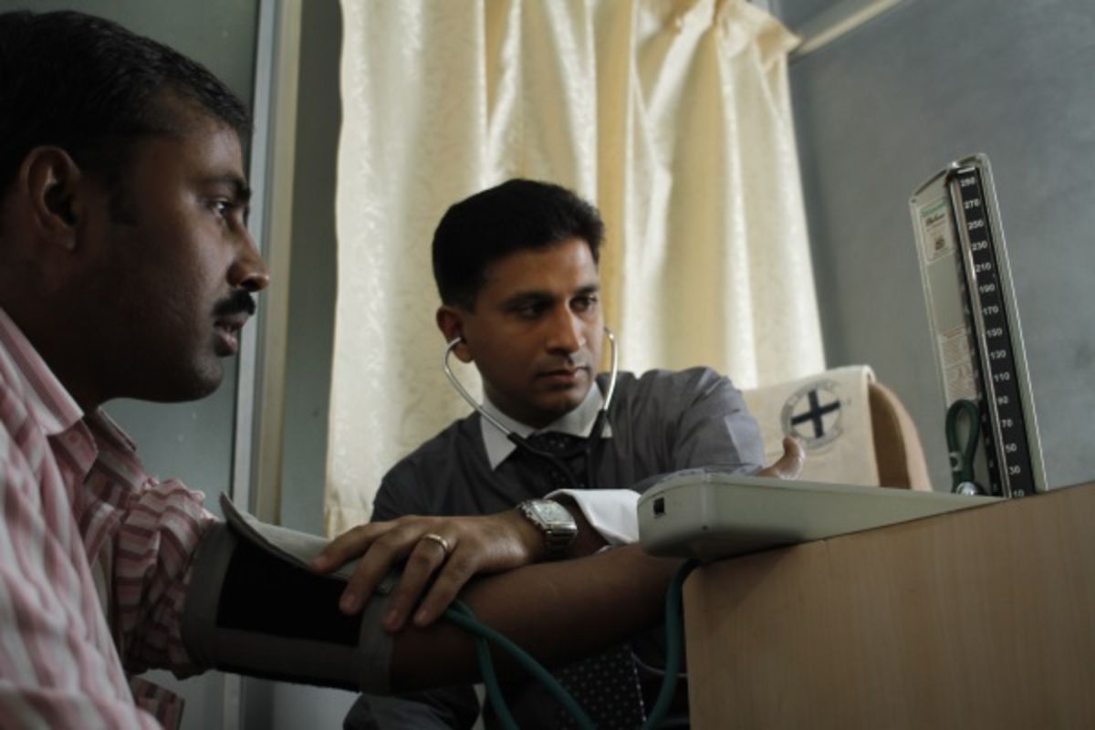 Doctor listening to patient’s pulse with stethoscope as both look at screen.